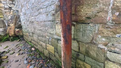 primer plano de una tubería oxidada contra una pared de piedra