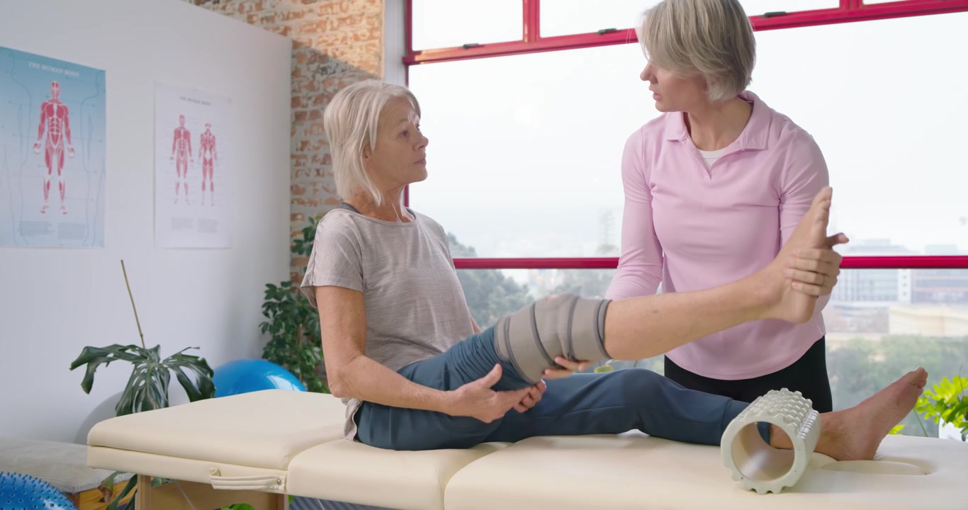Female physio placing foam roller wrapping knee and checking ROM while guiding extension at clinic
