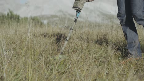 tracking shot of subject walking through mountain meadow grasses with metal detector