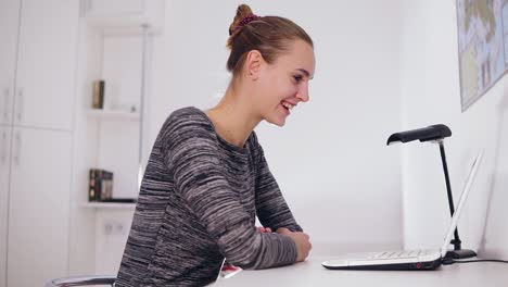 mujer sonriente feliz con computadora portátil teniendo videoconferencia en casa o en la oficina. ella está agitando la mano
