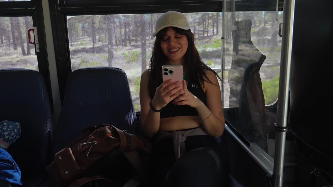 Mujer joven sonriendo y usando el teléfono mientras viaja en autobús