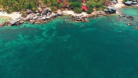 Aerial-drone-shot-of-a-tropical-beach-resort-surrounded-by-lush-greenery-and-crystal-clear-waters,-showcasing-a-serene-coastal-landscape-in-Thailand