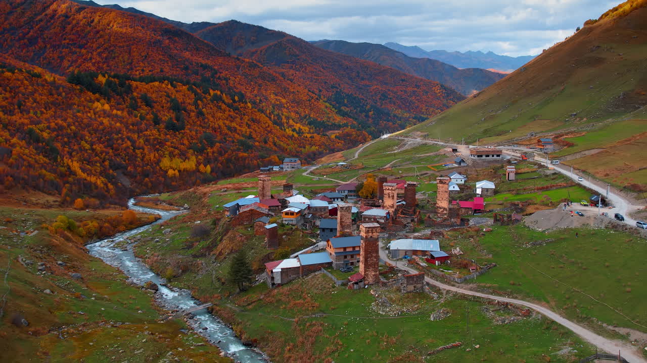 Sonbaharda rengarenk ormanlarla kaplı dağlardaki güzel küçük köye yaklaşırken. Uşguli, Yukarı Svaneti, Gürcistan drone görüntülerinden.