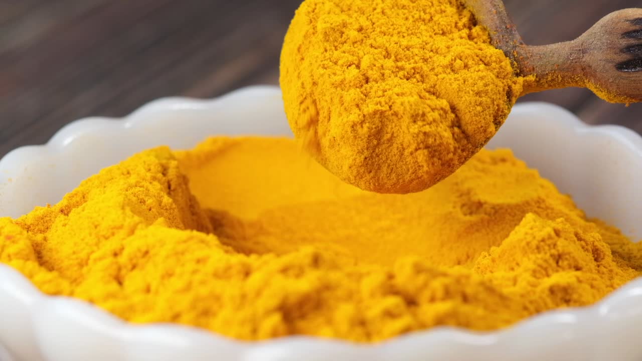 Turmeric Powder in a Bowl with Wooden Spoon