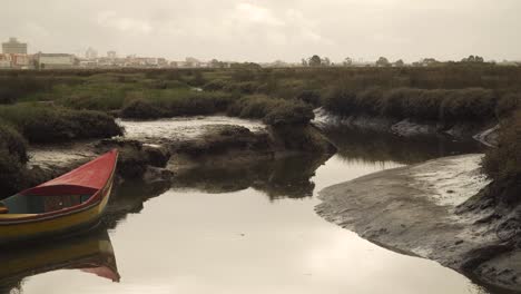 4K-old-wood-fishing-boat-stranged-on-the-muddy-banks-of-a-low-tide-river-with-Aveiro-city-in-the-background