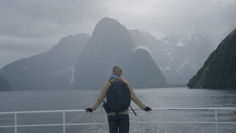 woman visiting milford sound standing on stern of tourist cruise ship, new zealand