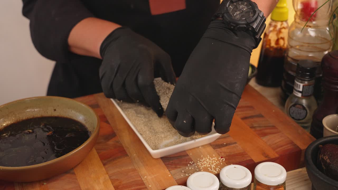 얼굴 없는 셰프가 두 손으로 연어 필레를 뒤집고, 모든 면에 흰 참깨를 바르고, 생선 필레를 가볍게 두드려 남은 흰 참깨를 뿌린 후 튀깁니다.