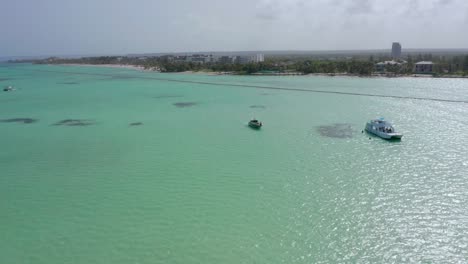 amazing exotic tropical waters of playa juanillio beach as white luxury motor boats and yachts sit anchored, dominican republic, drone aerial