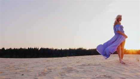 a slender woman in a light blue dress standing on the beach at sunset the wind plays with her dress