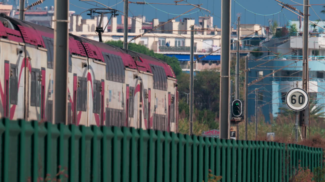 A regional double decker train moves through the French Riviera landscape, framed by electric lines and vegetation