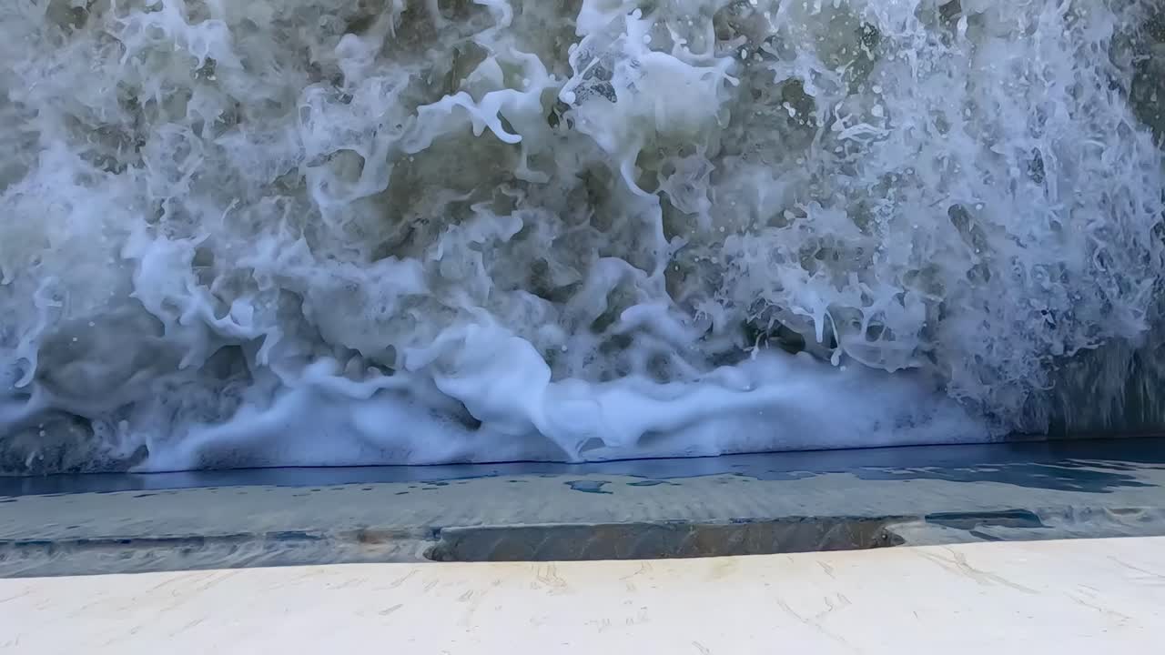 Close-up view of turbulent waves splashing against a concrete surface, creating dynamic foam patterns.