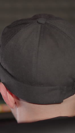 la cabeza de un hombre con una gorra negra, sentado en una silla negra, trabajando en una computadora. el ángulo de la cámara es desde atrás, mostrando al hombre centrado en su tarea mientras la cámara hace zoom