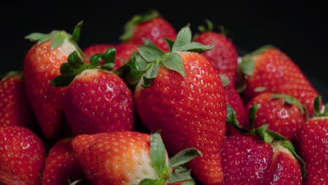 bright red strawberries piled on black background, closeup tilt down shot