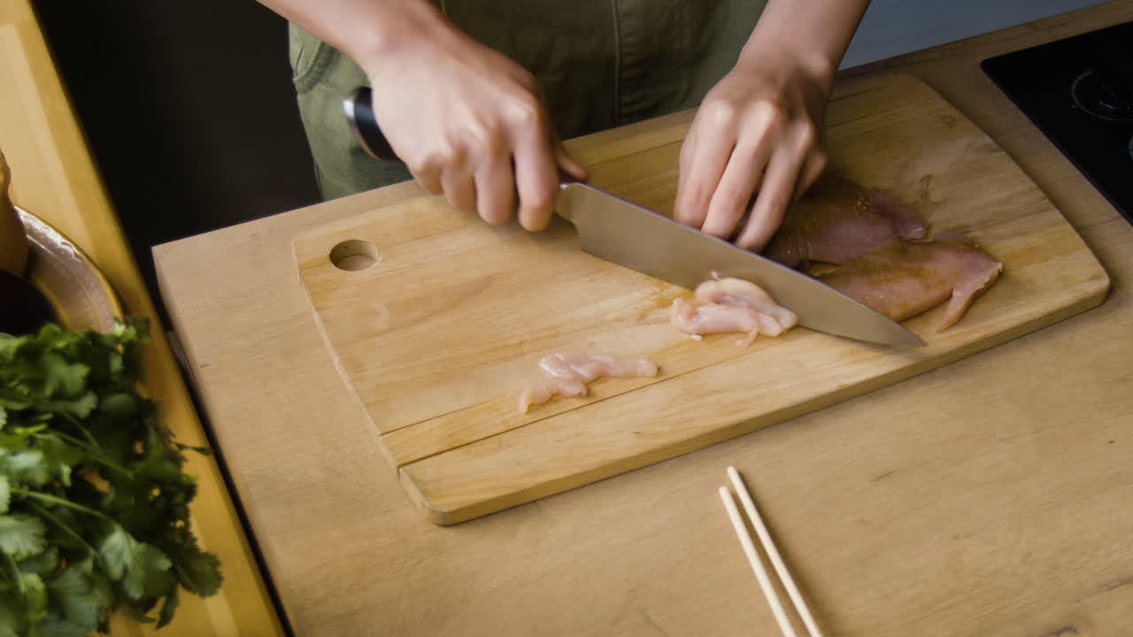 Person chopping raw chicken on a cutting board in a kitchen