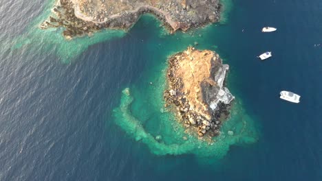 Aerial-drone-view-video-of-beautiful-boats-cruising-in-the-deep-blue-Aegean-sea-during-sunset,-Santorini,-Greece