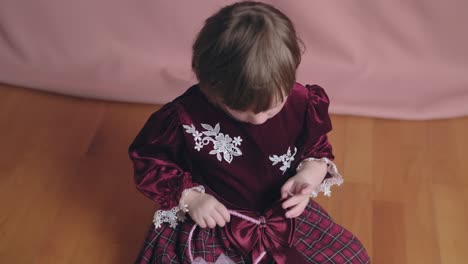 una niña linda en un vestido de borgoña vintage está jugando con un clip para el cabello