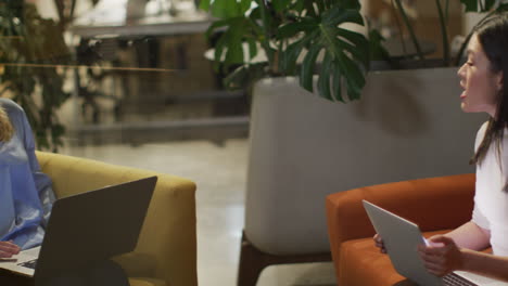 Asian-businesswoman-sits-on-an-orange-sofa-in-an-office,-with-copy-space