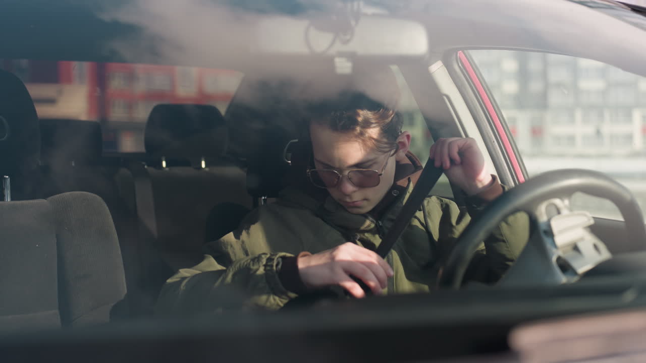 cab driver inside parked vehicle secures seatbelt and holds steering wheel while seated in winter setting with soft daylight casting gentle reflections through windshield onto car interior