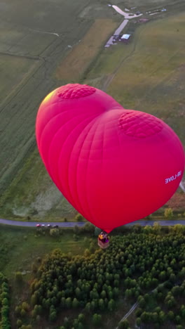 red aerostat over fields. romantic hot air balloon in a form of a heart travels in the sky on beautiful nature background at sunset. top aerial view. vertical video