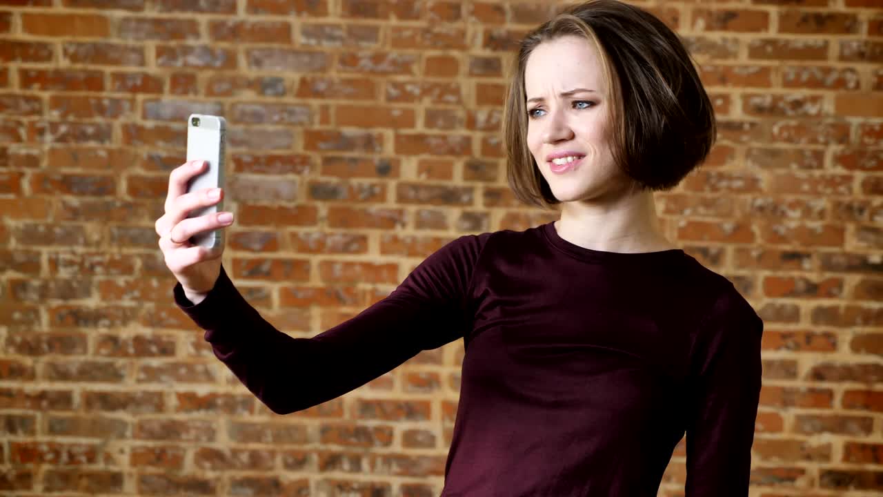 una joven hermosa tiene una llamada de video en su teléfono inteligente, sonriendo, concepto de comunicación, fondo de ladrillo