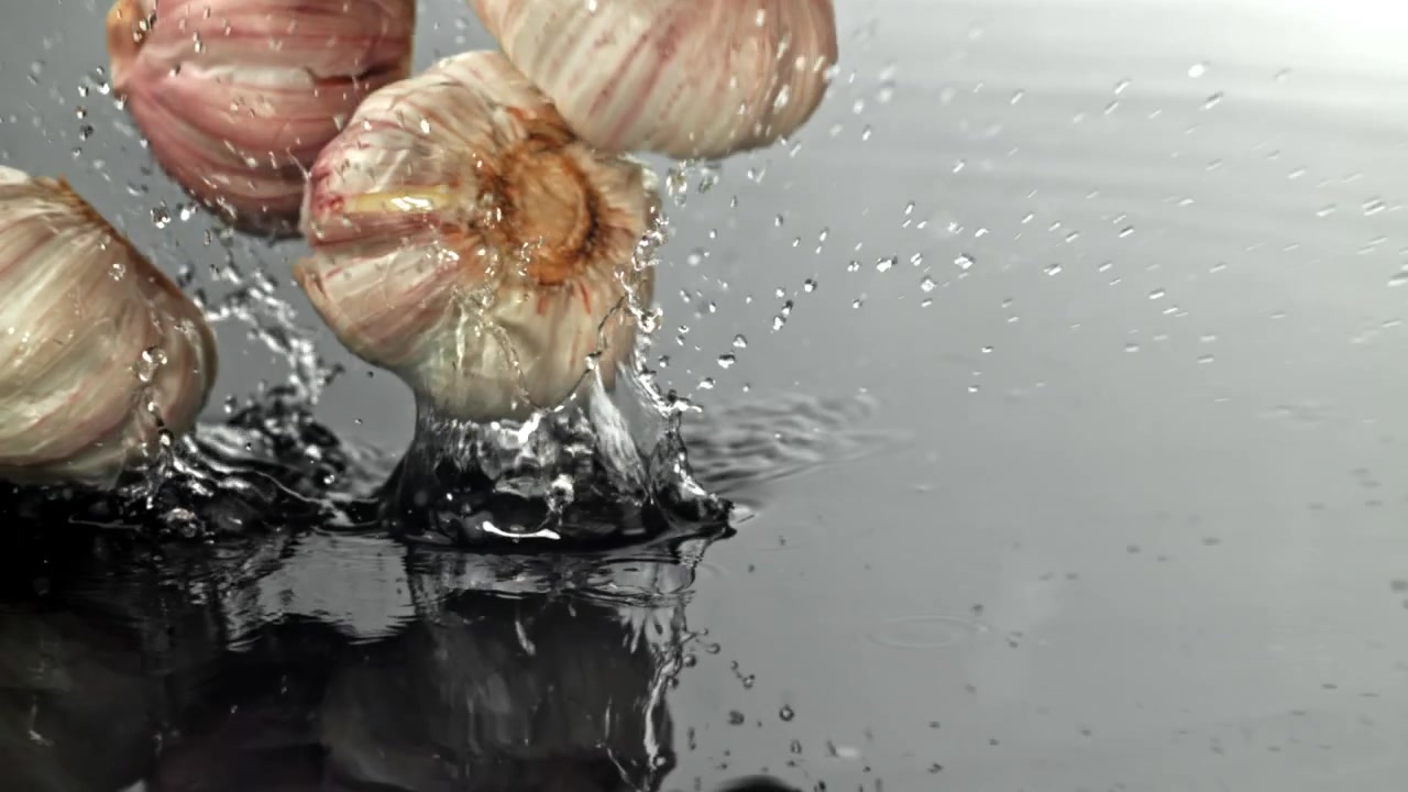 Teste d'aglio fresche che schizzano nell'acqua al rallentatore