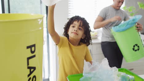 feliz hombre biracial y su hijo clasificando residuos en la cocina
