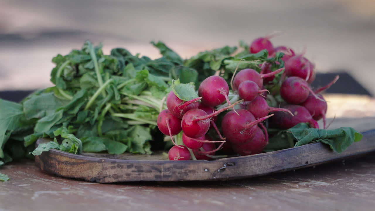 Still frame closeup clip of red radish group over wooden cutting board, with leafs still on, ready for cutting and chopping.