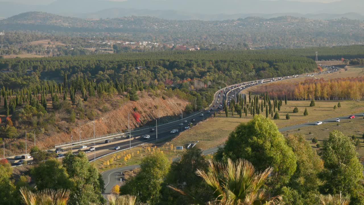 A wide-angle slow motion capture of cars navigating Canberra’s arterial roads. Trees in late autumn surround the weaving traffic.