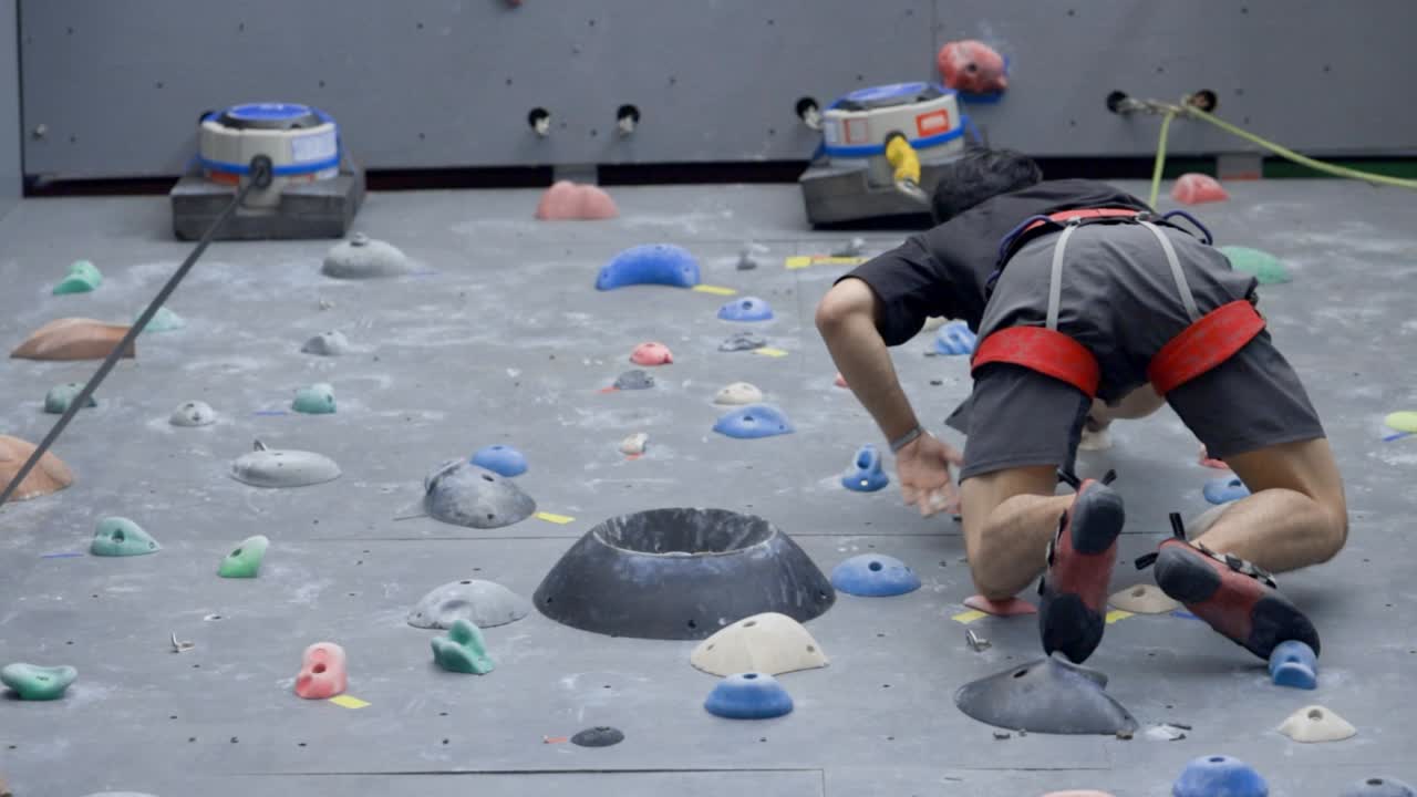 Asian man rock climbing indoors; look up shot