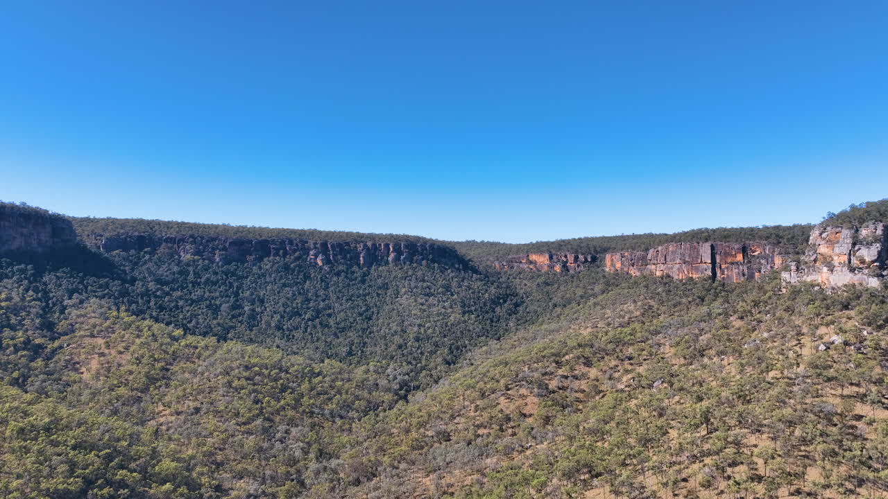 Aerial flies into the forested valleys and ancient cliffs of Cania Gorge National Park on a radiant fine blue day Monto Burnett Region Queensland Australia