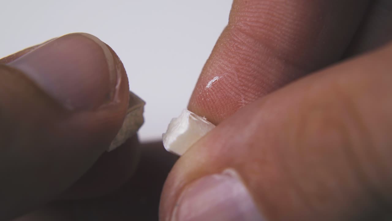 persona rompe la píldora blanca por la mitad en la macro de fondo claro