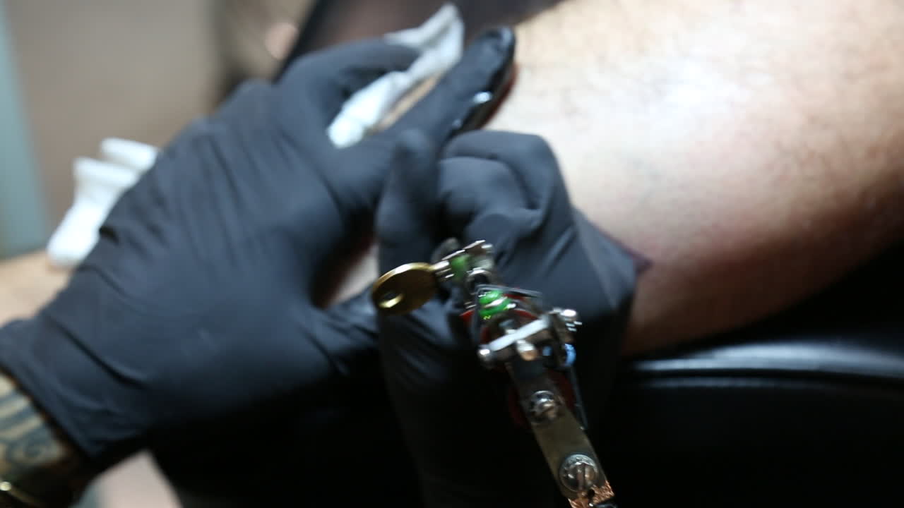 A close-up shot of a tattoo machine in action from the back of the tattoo gun as it inks a male client’s leg
