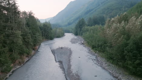 fast aerial footage flying over a grey river in between two banks of evergreen trees in the cascade mountains in washington