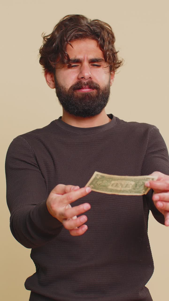 Poor man with insufficient amount of money holding one dollar banknote against beige background
