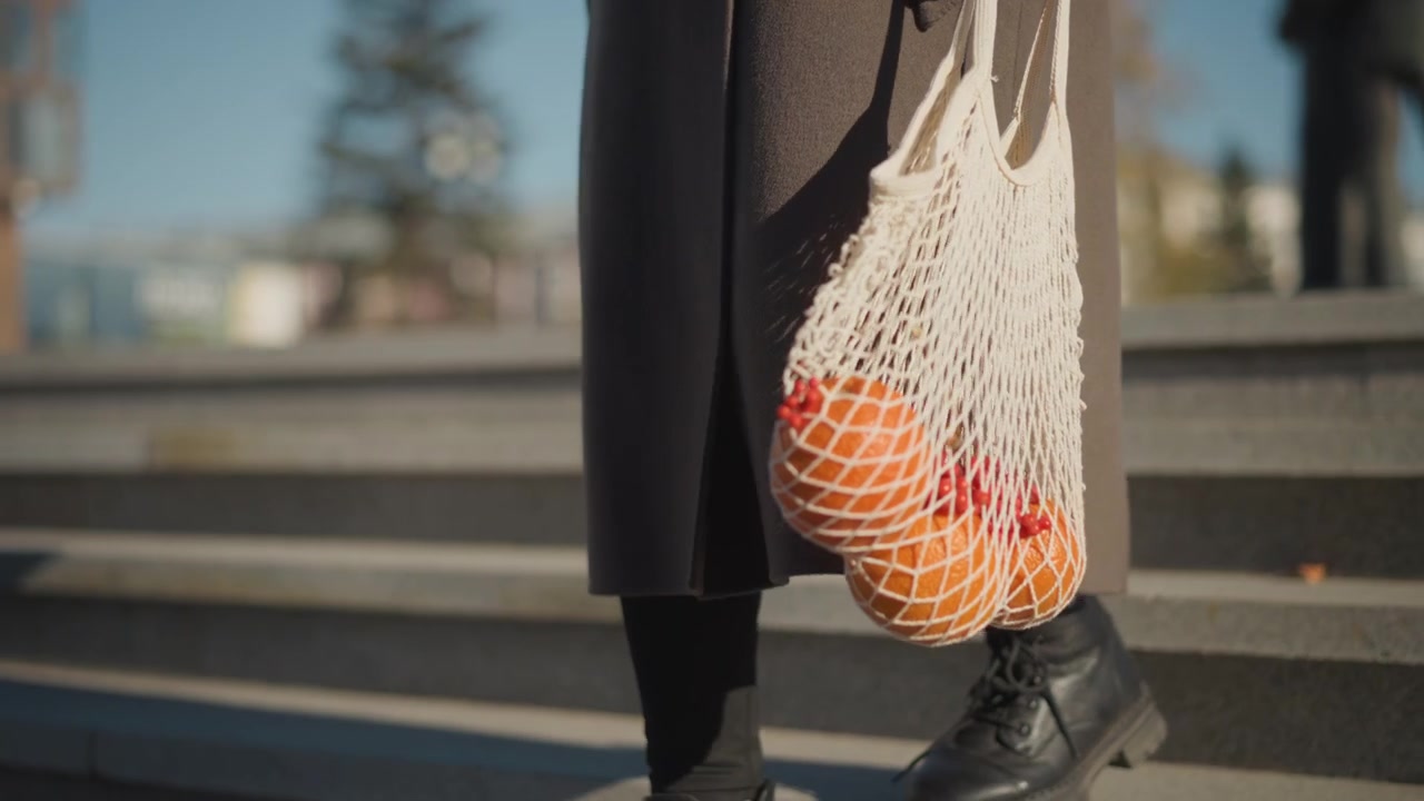 Donna che scende le scale trasportando una borsa a rete di arance