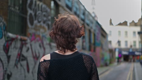 outdoor fashion portrait of young alternative style woman turning around and smiling walking along graffiti covered walls of london city street uk in real time 1