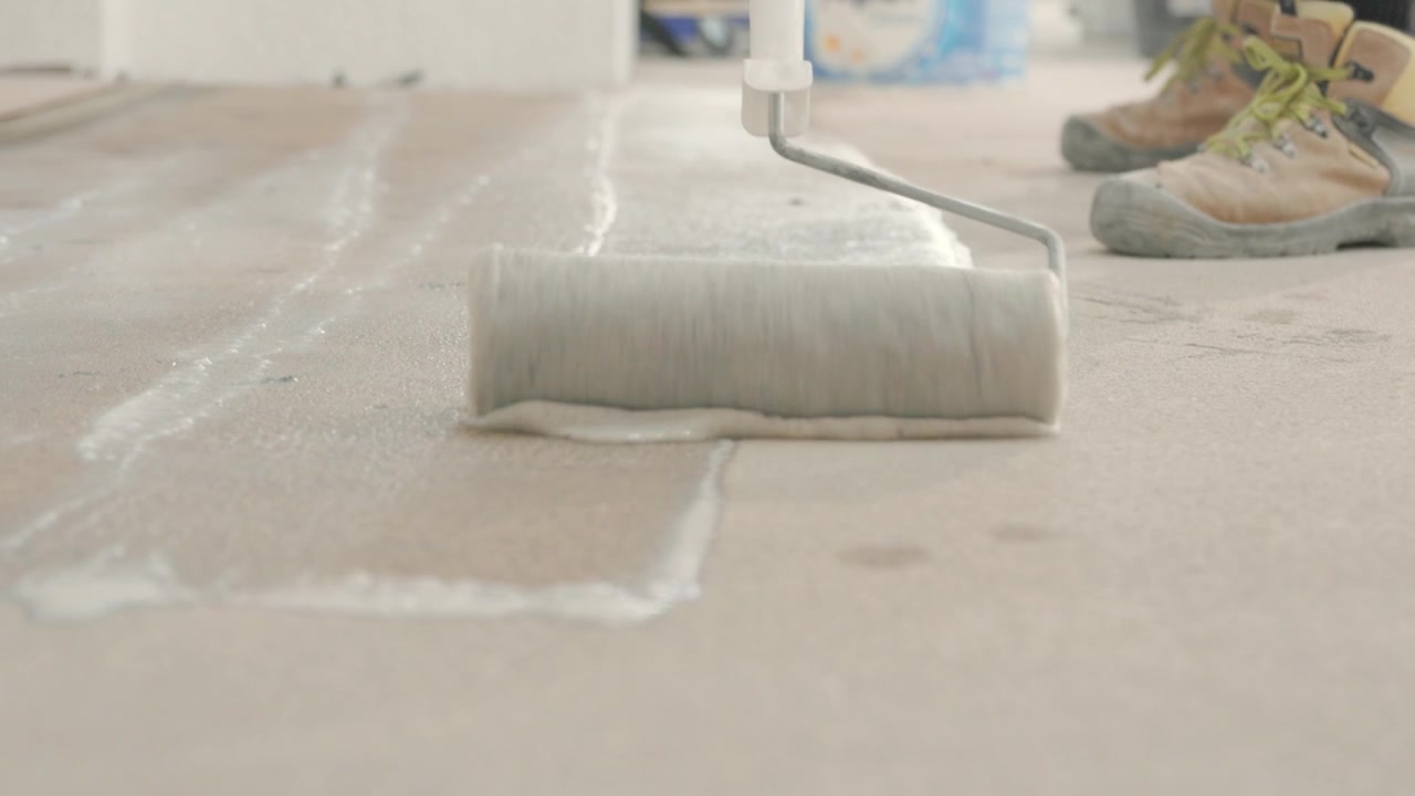 Spreading building material on the floor with a roller before installing tiles.