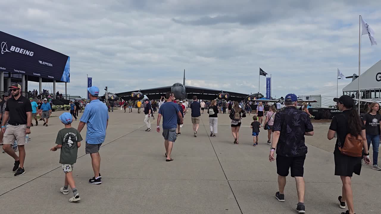 Airshow attendees walk near a Boeing B-52 bomber and exhibit booths on a cloudy day, enjoying displays and aviation attractions.