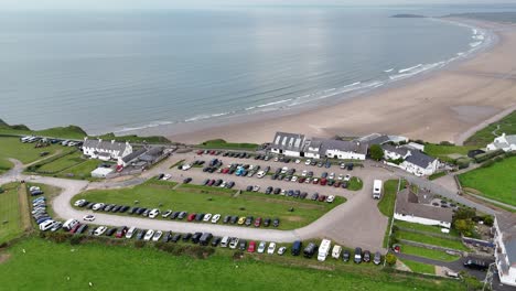 aerial drone view captures cars neatly arranged in parking lot in town by seascape at england, uk. the ocean glistens in sunlight, contrasting with orderly town and creating serene coastal scene