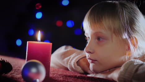 profile portrait of a girl looks at a burning candle and throws about it on christmas eve