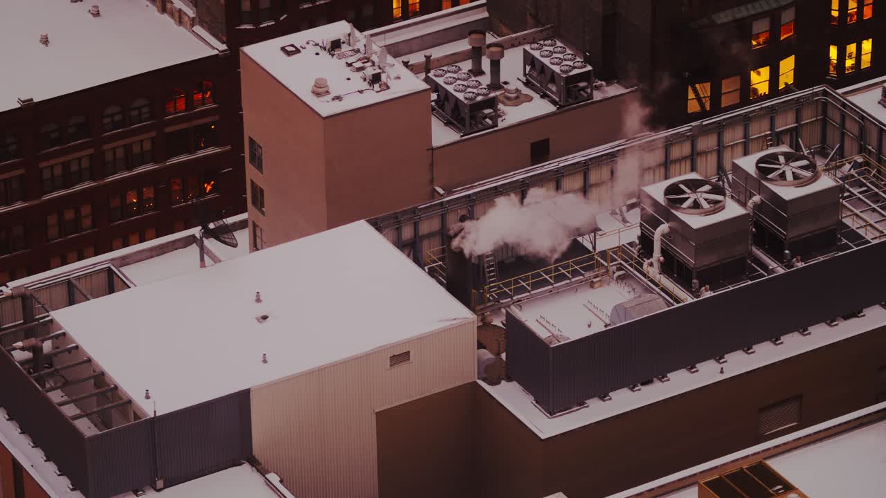 Telephoto view of snow-covered Chicago rooftops with industrial HVAC units releasing steam into the cold winter air at dusk