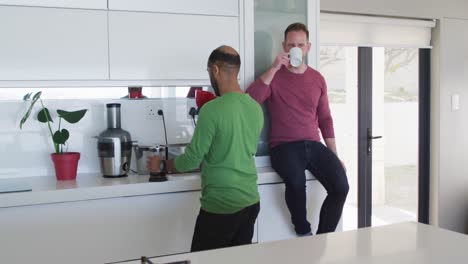 Multi-ethnic-gay-male-couple-drinking-coffee-in-kitchen