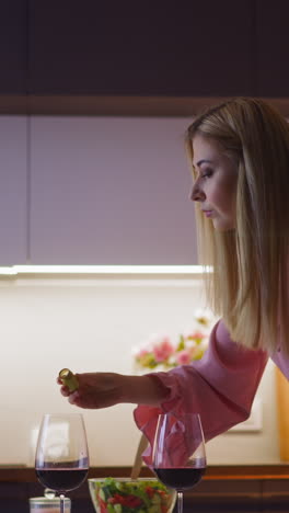 lady drink spiker pours soporific powder into glass with red wine of lover and looks into camera before romantic dinner in kitchen slow motion