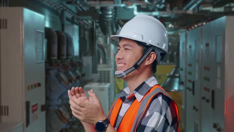 Close Up Side View Of Asian Male Engineer With Safety Helmet Smiling And Clapping His Hands While Standing In Engine Control Room, Work Of Electrical Generators