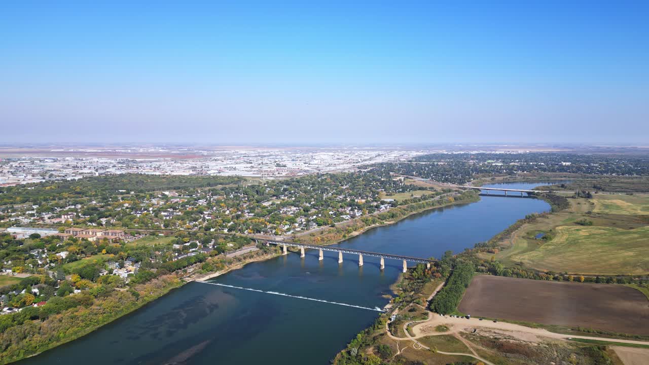 Slow forward aerial of Saskatoon in fall, blue sky, river side, bridges
