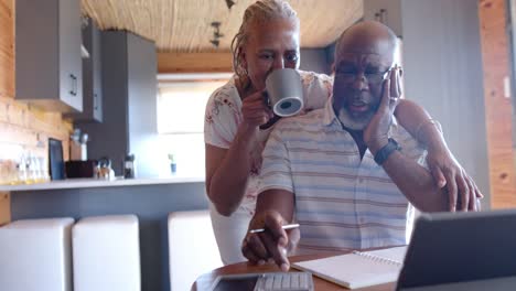 Senior-african-american-couple-embracing-and-doing-paperwork-using-tablet-at-home,-slow-motion