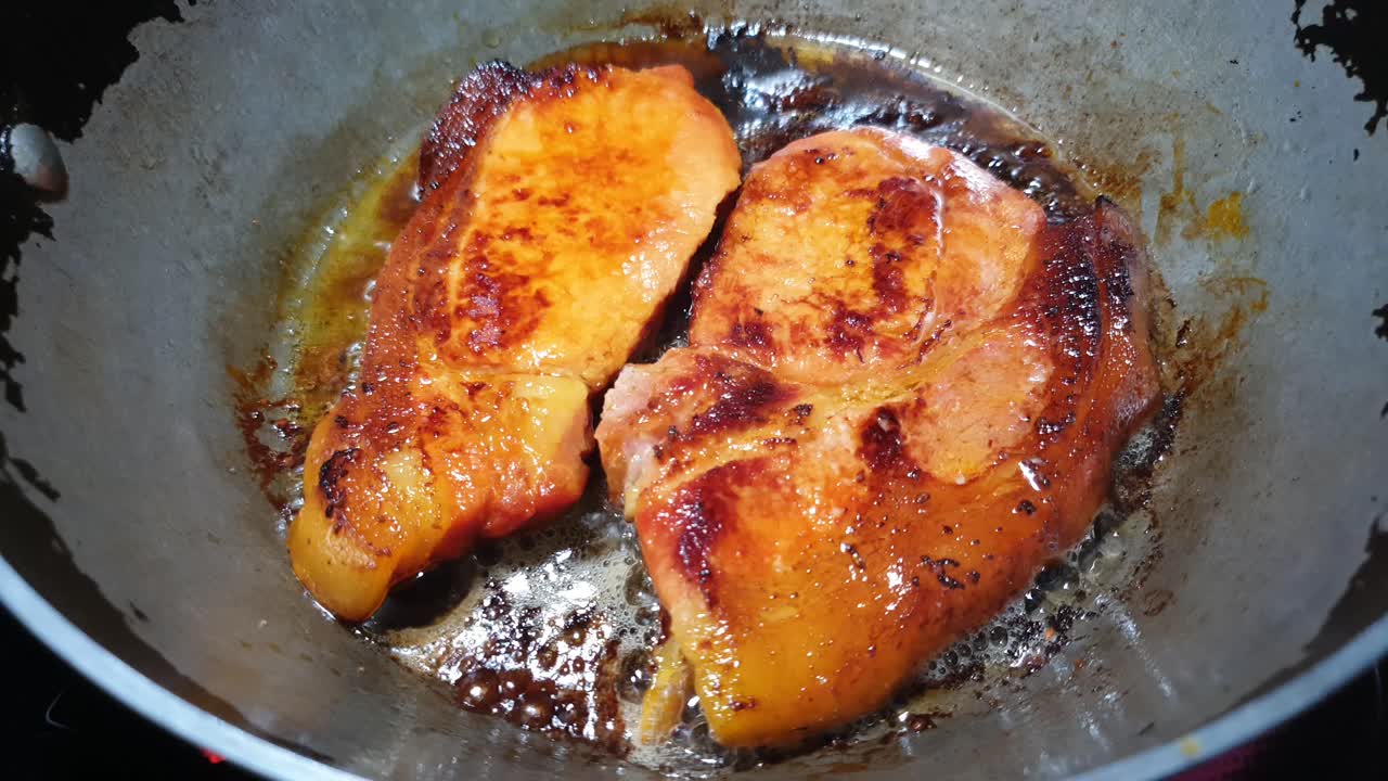 chisporroteando chuletas de tocino freír en mantequilla y aceite de oliva en una sartén de acero en la parte superior de la estufa de vidrio