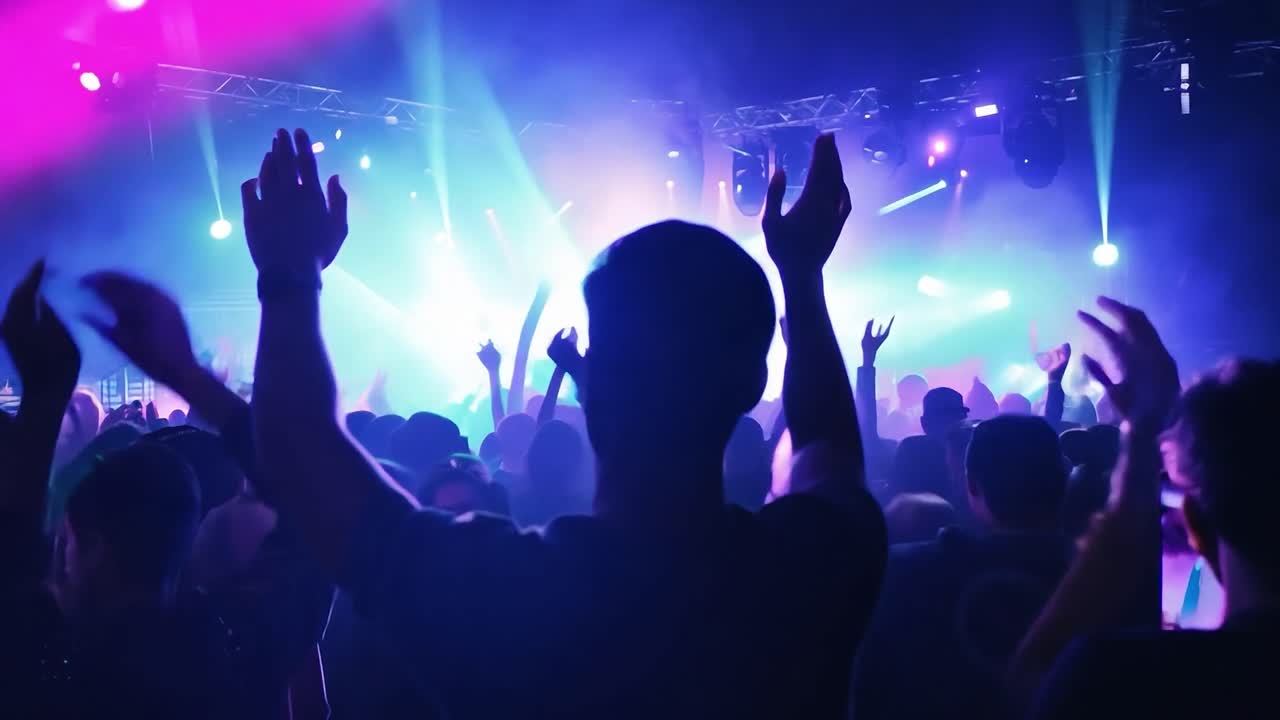Music fans raise their hands and cheer, reveling in the excitement of a live concert performance under vibrant lights