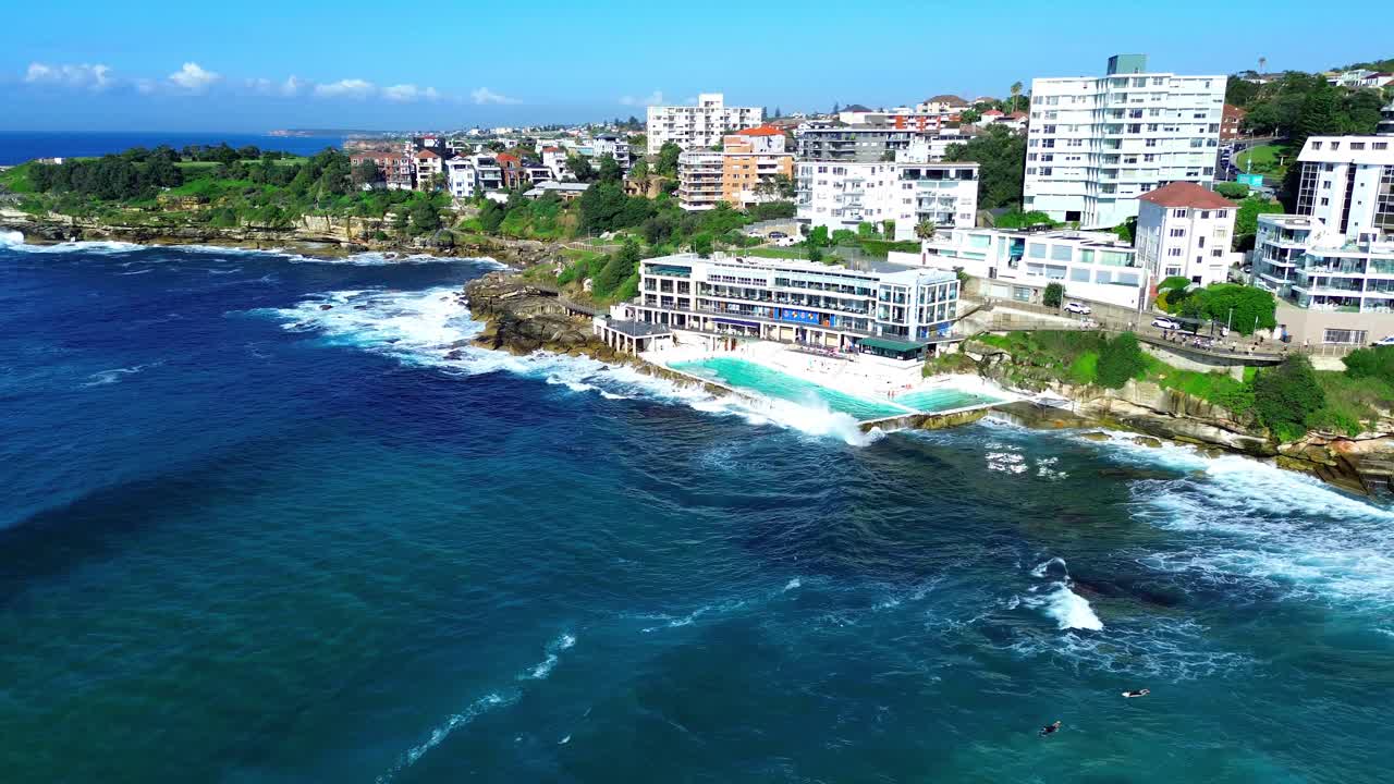 Aerial over sunny Bondi Beach coastline with ocean pool