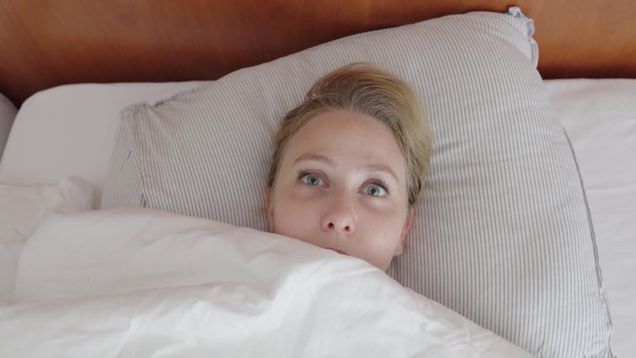 Close-up of a woman lying in bed, suddenly opening her eyes wide in shock. Her startled facial expression reflects fear, surprise or a bad dream
